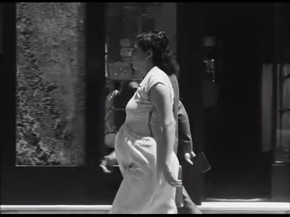 汽车经过街边时，一名穿浅色连衣裙、腹部明显隆起的女子从画面右侧走过