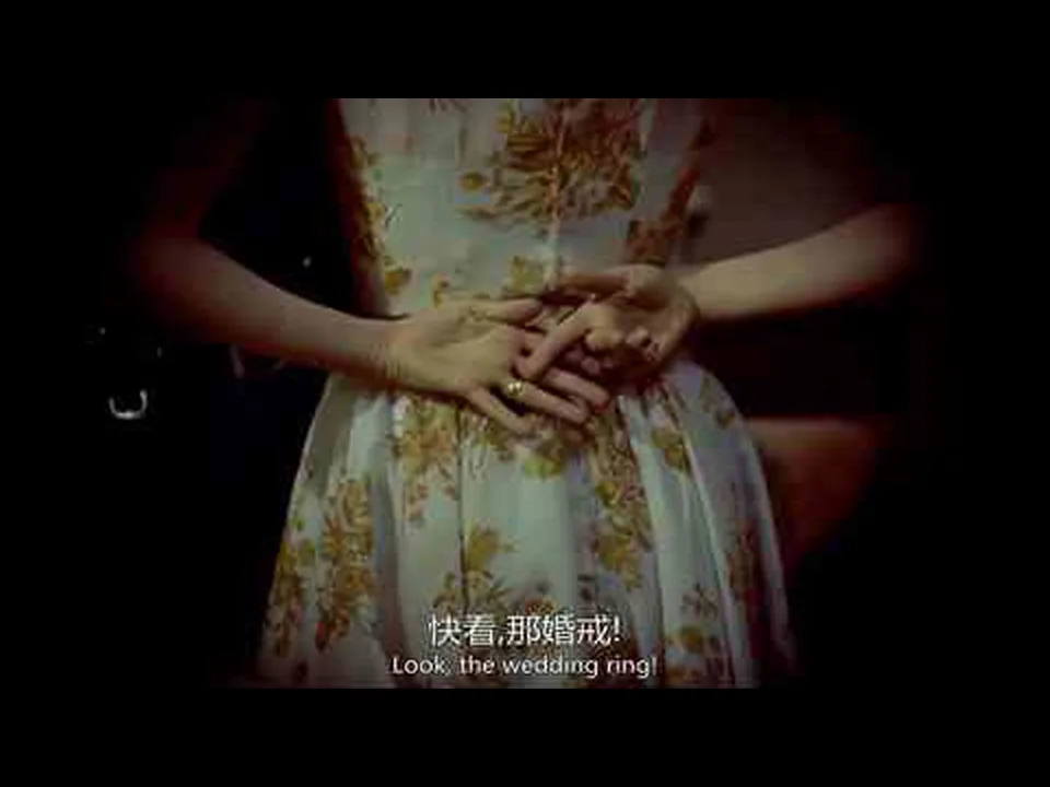 浅色花裙前,一只手的无名指戴着戒指,另一只手指向它;画面下方带中英文硬字幕。